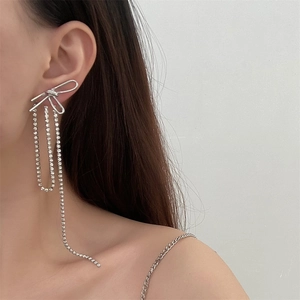 Detail of silver long bowknot tassel earrings with rhinestones worn by a model