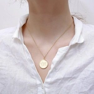 Close-up of a gold world map medallion necklace worn over a white textured linen shirt