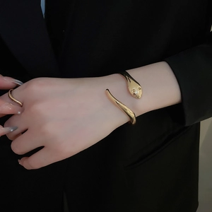 Polished gold snake bangle on a model's wrist against a black suit for a luxury look