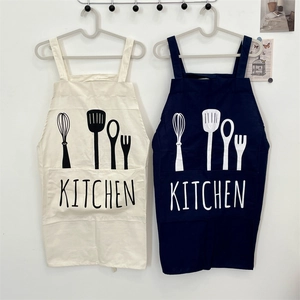 Detail of cotton linen kitchen aprons with front pockets and cutlery print hanging on a wall