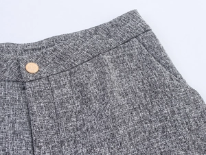 Detail of grey tweed fabric texture and decorative gold button on trousers waist