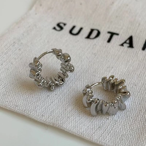 Detail shot of silver earrings with wavy texture on minimalist linen fabric