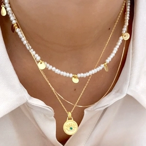 Layered gold necklace with evil eye pendant, green zircon, and white pearls on a model