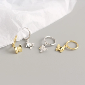 Detailed close-up of tiny butterfly hoop earrings in polished gold and silver finishes