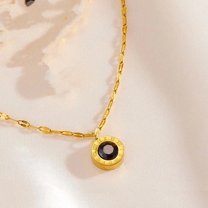Detail of gold-plated necklace featuring a round black stone pendant and Roman numerals