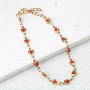 Dettaglio di un bracciale in acciaio inossidabile dorato con ciondoli a cuore in smalto rosso