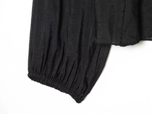 Vue détaillée de la manche de la blouse noire avec poignets élastiques et texture plissée fine