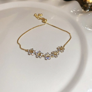 Close-up of golden flower bracelet with sparkling zircon petals on white ceramic plate
