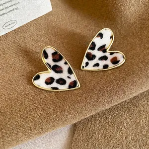Elegant heart-shaped leopard print earrings with gold frames on a brown textured background