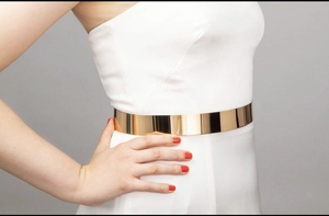 Close-up of polished gold mirror finish metal belt on a white dress for women