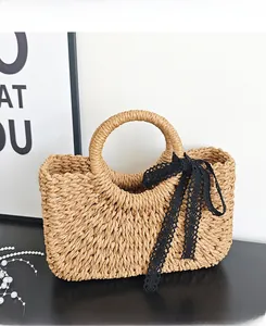 Detail of hand-woven straw tote bag featuring a black lace bow and sturdy round handles