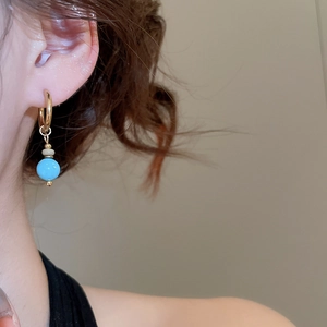 Close-up of vintage gold hoop earrings with round blue and beige turquoise stone pendants
