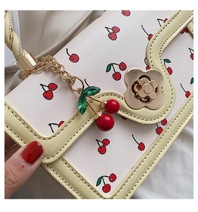 Detailed close-up of golden flower twist lock and cherry pendant on cream handbag