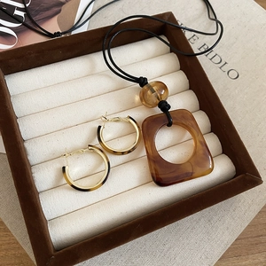 Close-up of leopard resin pendant necklace and gold hoop earrings in a velvet jewelry box