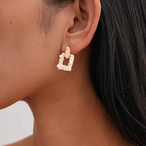Detailed view of square gold alloy drop earrings with faux pearls and rhinestones on model