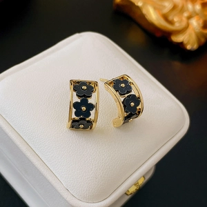 Detail of C-shaped gold earrings with black flowers on a white jewelry display box