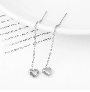 Detailed view of silver heart tassel ear threaders hanging on a white ceramic edge