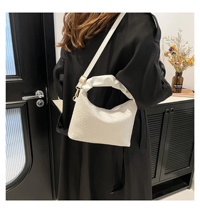 Detail of a white woven shoulder bag with gold hardware on a woman wearing a black coat