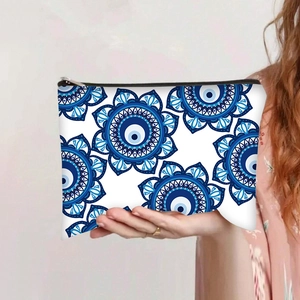 Detail showing hand holding evil eye cosmetic bag with blue mandala print and black zipper