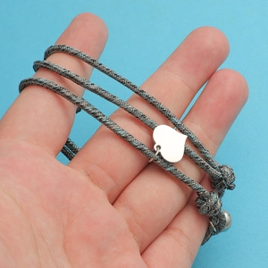 Detail of grey braided couple bracelets with silver heart charms and magnetic clasp
