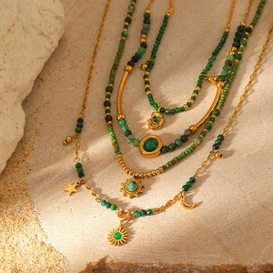 Layered gold chain necklace with green beads, sun and moon charms on a rocky background
