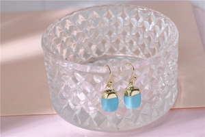 Close-up of blue stone square drop earrings on a glass rim with gold hooks