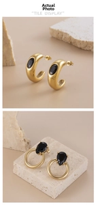 Detail of C-shaped gold earrings with black gemstone insets and water drop pendant style