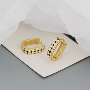 Detailed macro view of gold U-shaped earrings featuring black and white enamel checkerboard