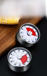 Mechanical stainless steel kitchen timer with red visual disk on wood background