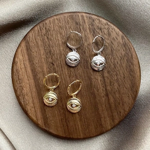 Detailed macro view of gold and silver evil eye hoop earrings with zircon on wood