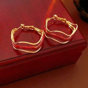 Close-up of golden wavy hoop earrings with red enamel detail on a dark wooden box