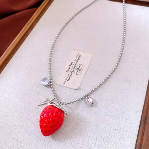 Macro detail of strawberry pendant necklace with heart stones on white tray
