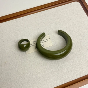 Close-up of olive green resin ring and open cuff bracelet on textured beige fabric