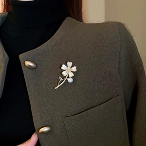 Vue détaillée d'une broche fleurie en perles sur le revers d'un blazer vert