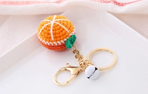 Detailed view of handmade knitted orange keychain with golden metal clasp and white bell