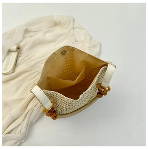Detail view of woven straw bucket bag showing fabric lining, inner pocket and wood bead handle