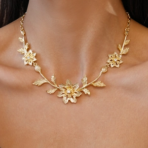 Close-up of elegant gold leaf and flower necklace worn by a model in soft lighting