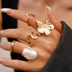 Nahaufnahme eines 5-teiligen goldfarbenen Blumenring-Sets mit Perlen auf einer Hand
