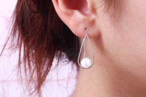 Close-up of S925 silver teardrop earrings with a white pearl on a female model