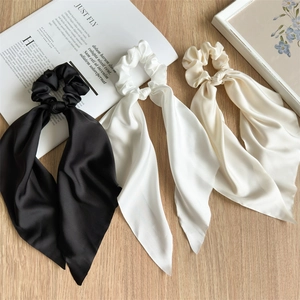 Three satin ribbon scrunchies in black, white and beige on a wooden background