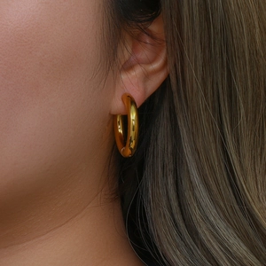 Detail shot of a model wearing 18K gold plated thick stainless steel hoop earrings