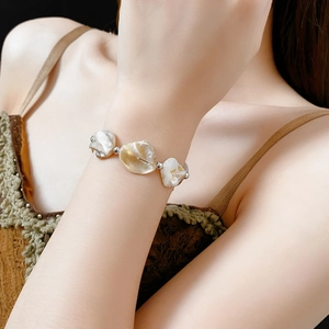 Gros plan d'un bracelet en coquillages irréguliers avec accents dorés sur le poignet