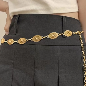 Detail of vintage gold metal waist chain with engraved oval medallions on a model
