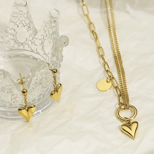 Detail of a golden double-layered heart necklace and matching earrings set on tray
