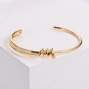 Polished gold knot open bangle bracelet minimalist style on white geometric cubes