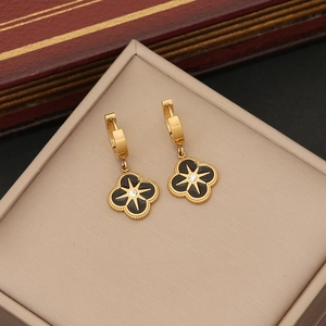 Golden clover earrings with black enamel, clear gemstone, and beaded edges in a jewelry box