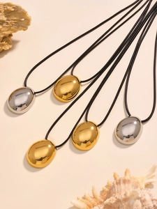 Macro shot of polished gold and silver teardrop pendants with black woven cord