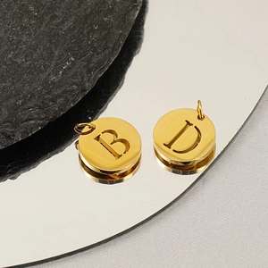 Polished gold stainless steel hollow letter B and D pendants on a reflective mirror base