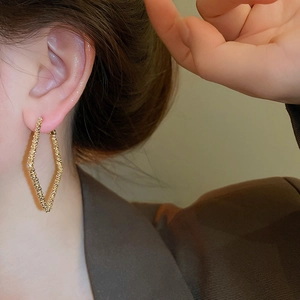 Detail of gold geometric earrings showing textured metallic finish on female model