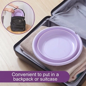 Purple collapsible washbasin for travel placed on top of clothes in an open suitcase